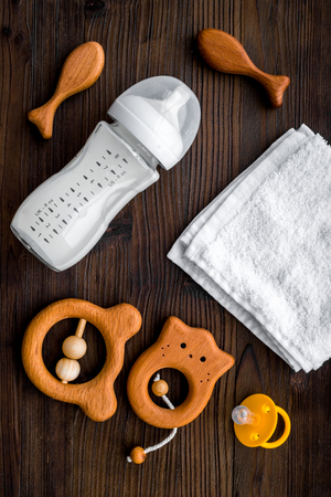 Baby accessories. Wooden toys, pacifier and bottle on dark wooden background top view.の写真素材