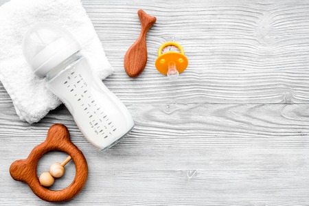 Baby accessories. Wooden toys, pacifier and bottle on grey wooden background top view.の写真素材
