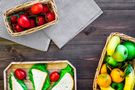 What bring for a picnic. Sanwiches, fruits, vegetables on tablecloth on dark wooden background top view.の写真素材