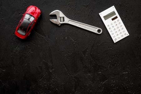 Price of car repair. Wrench near car toys and calculator on black background top view.の写真素材