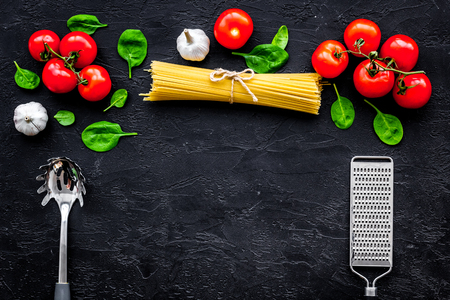 Italian pasta concept. Spaghetti, tomatoes, garlic, cheese grater, spoon for spaghetti on black background top view.の写真素材