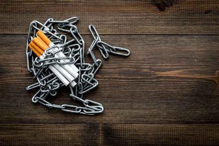 Quit smoking. Cigarettes in chains on dark wooden background top view.の写真素材