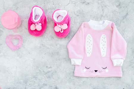 Cute pink baby clothes for girl. Shirt, booties, toy, bottle on grey background top view copy spaceの写真素材