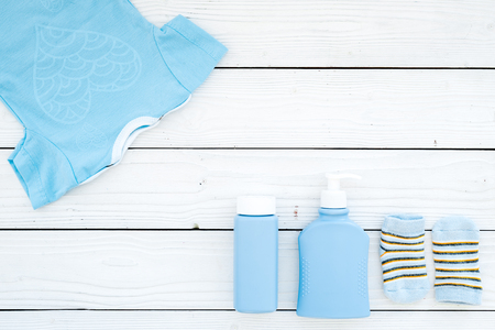 Cute blue baby clothes for boy. Bodysuit, socks, cosmetics on white wooden background top view copy spaceの写真素材