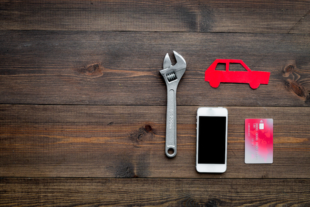 Looking for automobile service online. Cost calculation. Pay for car repair. Car silhouette, wrench, cell phone, bank card on dark wooden backgound top view.の写真素材