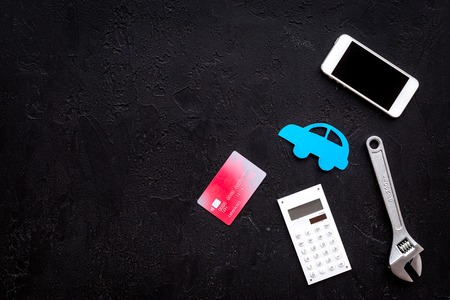 Cost of car repair. Automobile service. Car silhouette, wrench, cell phone, bank card on black backgound top view.の写真素材