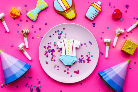 Celebrate child's birthday. Cookies in shape of baby accesssories, party hats, gift box, confetti on pink background top view.の写真素材