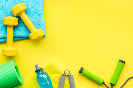 Fitness background. Equipment for gym and home. Jump rope, dumbbells, expander, mat, water on pastel yellow background top view space for textの写真素材