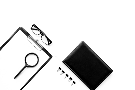 Strict monochrome white and black office desk table with pad, magnifier, notebook, glasses on white background top view copy spaceの写真素材