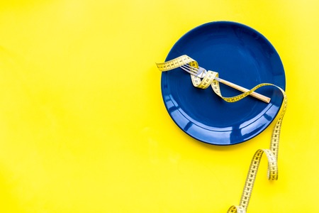 Medical starvation for lose weight. Empty plate, apple and measuring tape on bright yellow...
