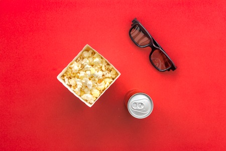 Cinema snacks. Popcorn in paper bag and soft drink near glasses on red background top view copy spaceの写真素材