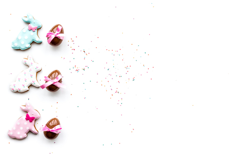 Sweets for Easter table. Chocolate eggs near cookies in shape of Easter bunny on white background...