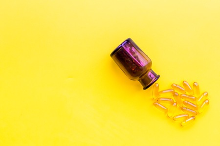 Color pills spilling out of a pill bottle on yellow background top view.の写真素材