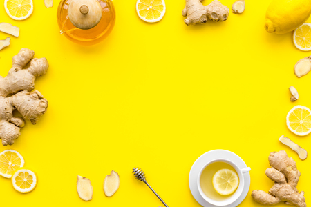 Warming tea with lemon and ginger. Cup, teapot, ginger root on yellow background top view copy space