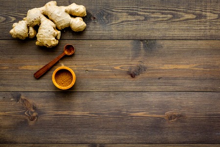 Spice and condiment. Ground ginger in small bowl near ginger root on dark wooden background top view copy spaceの写真素材