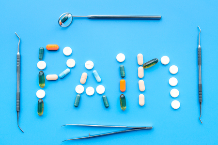 Toothache, dental pain. Fear of dental treatment. Word pain lined with pills near dentist tools. Blue background top viewの写真素材