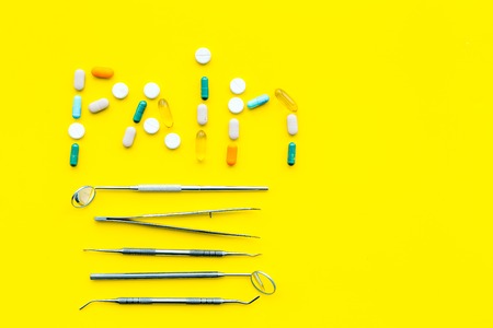 Toothache, dental pain. Fear of dental treatment. Word pain lined with pills near dentist tools. Yellow background top view copy spaceの写真素材