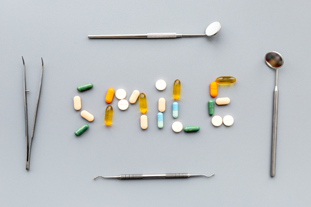Prevention of diseases of the oral cavity. Healthy smile. Dentist appointment. Word smile lined with pills near dentist tools. Grey background top viewの写真素材
