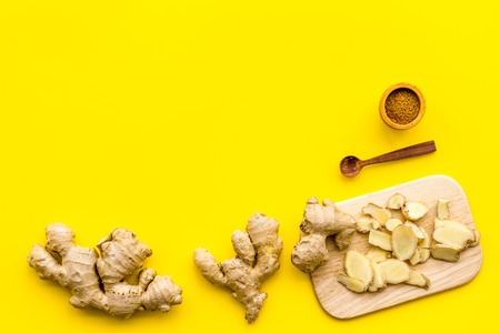 Spice and condiment. Ground ginger in small bowl near sliced ginger root on cutting board on yellow background top view.の写真素材