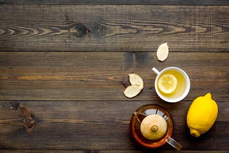 Tea for cure colds. Cup, teapot, ginger root and lemon on dark wooden background top view.の写真素材