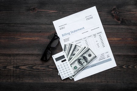 Paying bills. Billing statement near calculator, money, glasses on dark wooden background top view copy spaceの写真素材