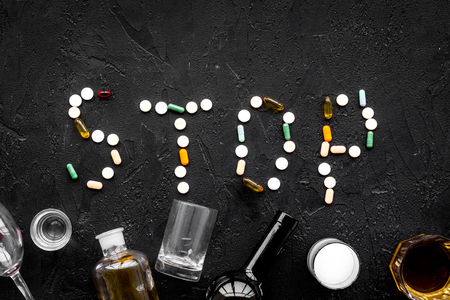 Stop alcohol. Word stop lined with pills near glasses and bottles on black background top view.の写真素材