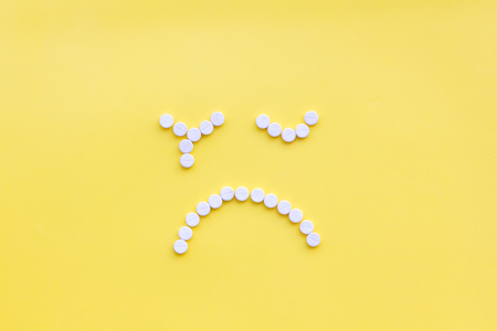 Emotion management concept. Overcome depression. Sad face lined with pills. Yellow background top view copy spaceの写真素材