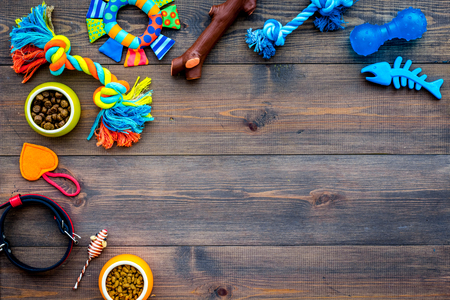 Pet accessories. Toys near bowls with animal feed, collar on dark wooden background top view.の写真素材
