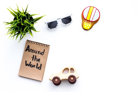 Family trip concept. Sun glasses, green plant, air ballon cookie, car toy. Around the world hand lettering in notebook on white background top view copy spaceの写真素材