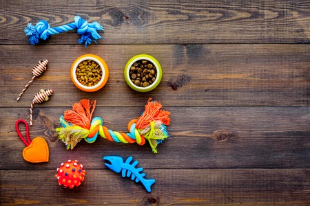 Pet care concept. Toys near bowls with animal feed on dark wooden background top view.の写真素材