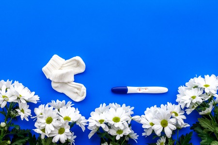 Joy of long-awaited pregnancy. Pregnancy test with two stripes near flowers on blue background top view.の写真素材