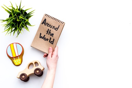 Family trip concept. Green plant, air ballon cookie, car toy. Around the world hand lettering in notebook on white background top view copy spaceの写真素材