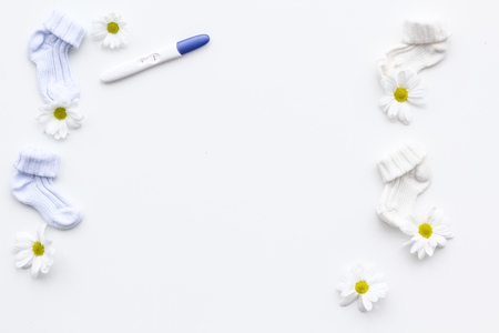 Pregnancy and preparation for childbirth. Pregnancy test near booties and flowers on white background top view copy spaceの写真素材