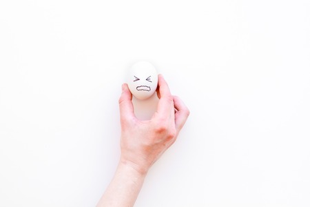 Emotion management concept. Suppression anger. Angry face drawn on egg. White background top view...