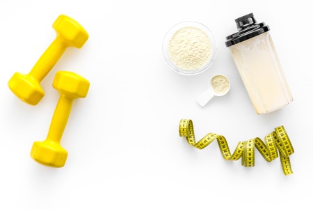 Nutrition for muscle growth. Scoop of protein near shaker and dumbbell on white background top view.の写真素材