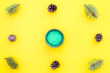 Pine spa cosmetics, products for skin care. Green aromatic spa salt near branches and cones on yellow background top view copy spaceの写真素材