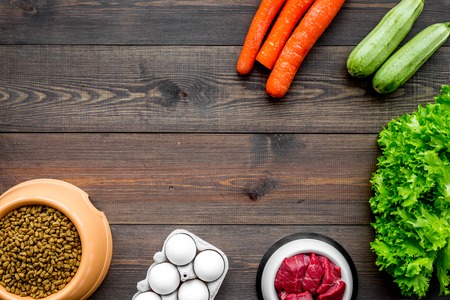 Dry pet food with natural ingredients. Raw meat, vegetables zucchini and carrot near eggs on dark wooden backgroud top view copy spaceの写真素材