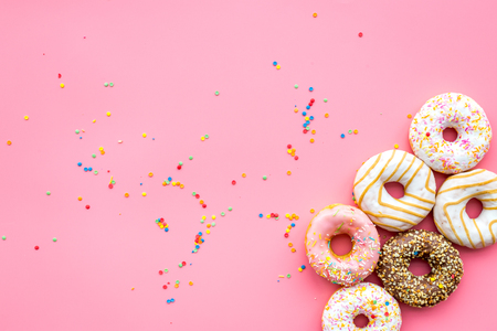 Donuts decorated icing and sprinkles on pink background top view copy space patternの写真素材