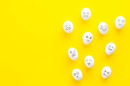 Emotions in communication at social media. Faces drawn on eggs. Happy, smile, sad, angry, in love, saticfied, laughing. Yellow background top view copy spaceの写真素材