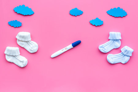Joy of long-awaited pregnancy. Pregnancy test with two stripes near socks on pink background top view mock-up.の写真素材