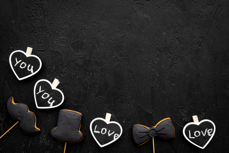 Mens birthday concept. Cookies in shape of moustache, hat, bow tie. Hearts with lettering love you on black background top view copy spaceの写真素材