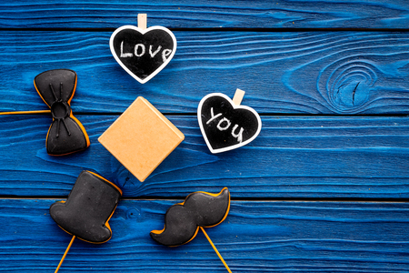 Gift for man on birthday. Gift box among cookies in shape of moustache, hat, bow tie and hearts with lettering love you on blue wooden background top view.の写真素材