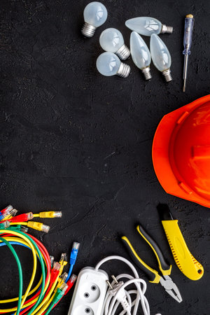 Electrician work concept. Hard hat, tools, cabel, bulb, socket outlet on black background top view...