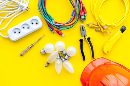 Electrician work concept. Hard hat, tools, cabel, bulb, socket outlet on yellow background top view