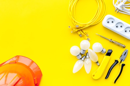 Electrician work concept. Hard hat, tools, cabel, bulb, socket outlet on yellow background top view copy spaceの写真素材