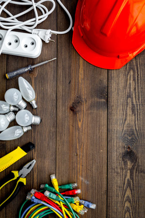 Electrician work concept. Hard hat, tools, cabel, bulb, socket outlet on dark wooden background top...