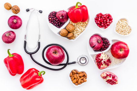 Products good for heart and blood vessels. Vegetables, fruits, nuts in heart shaped bowl near stethoscope on white background top view.の写真素材