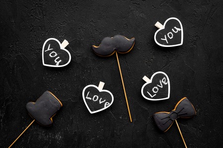 Men's birthday concept. Cookies in shape of moustache, hat, bow tie. Hearts with lettering love you on black background top view.の写真素材