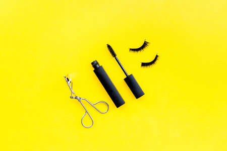 Makeup set for expressive eyelashes. Mascara, false eyelashes, eyelash curler on yellow background...