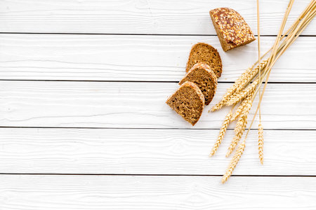 Appetizing fresh bread concept. Sliced loaf near ears of wheat on white wooden background top view.